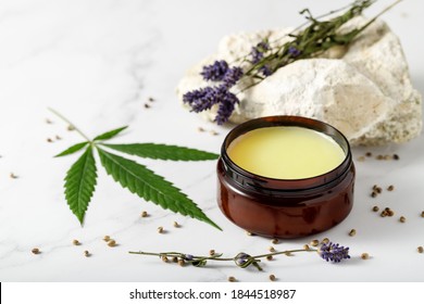 Composition with cannabis healing  wax salve or cream with  lavender extract, flowers, hemp leaves  and seeds on marble background with copy space - Shutterstock ID 1844518987