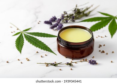 Composition with cannabis wax salve or cream with  lavender extract, flowers, hemp leaves  and seeds on marble background with copy space. Cannabis products - Shutterstock ID 1939345441