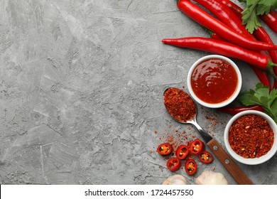 Composition with chilli pepper, powder spice, garlic and sauce on gray background