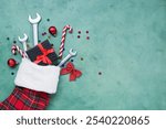 Composition with Christmas sock, gift box and wrenches on green background