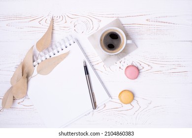Composition from a clean diary for your text, fountain pen, a cup of coffee, macaroons and beige eucalyptus leaves on a whitewashed wooden table. Flat lay.