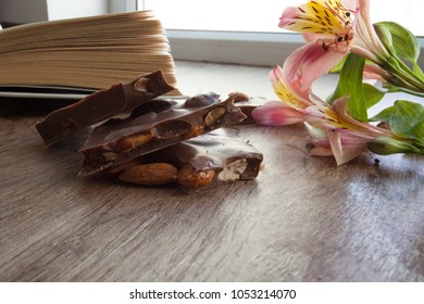 Composition consists with pieces of milk chocolate, open book and flower by the window in the daylight provides dreamy mood - Shutterstock ID 1053214070