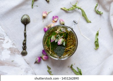 Composition with cup of herbal tea with mint and vintage spoon. Dry leaves and flowers as decor, light background. Flat lay, top view