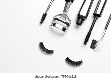 Composition with curler and false eyelashes on white background