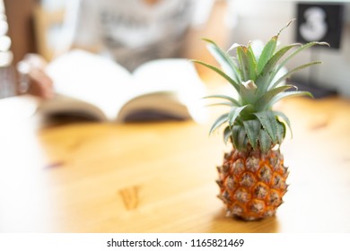 Composition with delicious small pineapple   on wooden beach table.People read book blur.