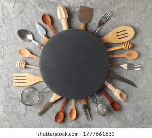 Composition with different kitchen cutlery and round cutting board on gray background