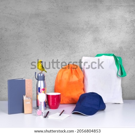 Composition of different promo products rich colors -Thermo mug-pens-mug-notebook-cap-notepaper-Backpack-tote bag canvas -exotic bird.
