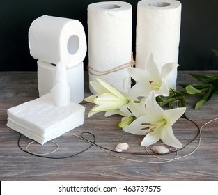 Composition Of Disposable Paper Hygienic Products On Wooden Table Against Black Background With Lilies And Sea Shells. Concept Of Purity And Spa.