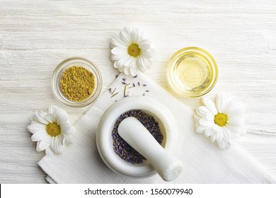 Composition with dried lavender flowers in white marble pestle and mortar and natural chamomile oil cosmetic in glass jar on white background, top view with free copy space