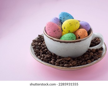Composition with easter eggs in cup surrounded by coffee roasted beans. Easter coffee concept. Mug full of colorful eggs on a plate with coffee beans on a pink background with copy space.