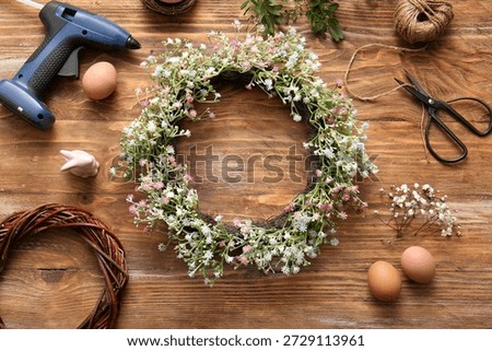 Composition with Easter wreath, flowers, eggs and scissors on wooden background