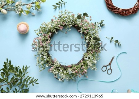 Composition with Easter wreath, green twigs, flowers and egg on blue background