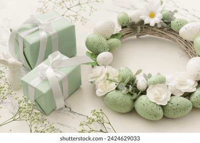 Composition with Easter wreath made of green painted eggs and bunny figurine and gifts on white table