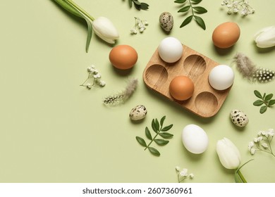 Composition with egg holder, Easter eggs, green leaves and feathers on green background