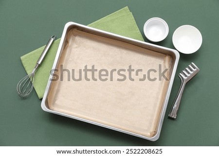 Composition with empty baking tray, bowls, whisk and tongs on color background