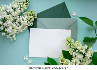 Composition with empty green envelope and beautiful spring lilac flowers on mint background. Mockup card invitation greeting card postcard copy space template. Branches of lilac blooming bouquet. 