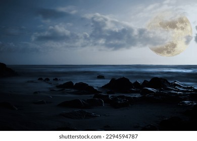 Composition with full moon at night, empty beach, sea and glowing rocks