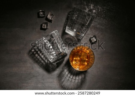 Composition with glass of cold rum, empty glasses and ice cubes on grey grunge background