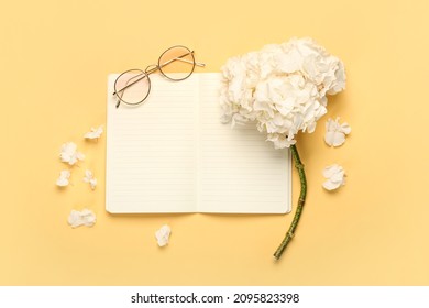 Composition with hydrangea flower, blank notebook and glasses on color background