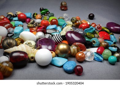 Composition Of Jewelry Making Supplies, Colorful Shiny Mixed Beads, Pliers And Craft Wire On A Gray Fabric Background, Close Up.