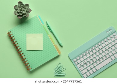 Composition with keyboard, notebook and paper clips on green background.Top view