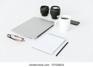 composition with laptop, notepad, camera lenses and cup of coffee on white tabletop