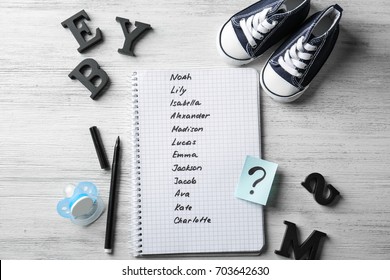 Composition with list of baby names in notebook on wooden background