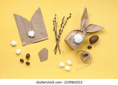 Composition With Materials For Making Easter Bunny Gift Bags, Chocolate Eggs And Pussy Willow Branches On Yellow Background