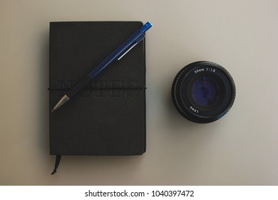Composition with a mechanical pencil, a notebook and a camera lens.