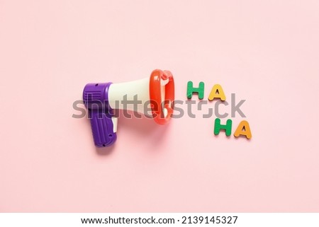 Composition with megaphone and text HA HA for April Fools Day celebration on pink background