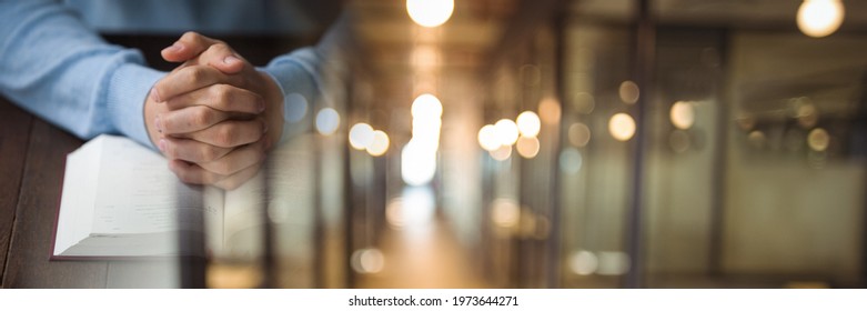 Composition of midsection of man praying with holy bible open with blurred corridor. religion and tradition concept digitally generated image.