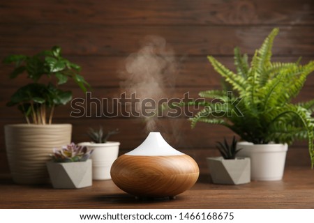 Composition with modern essential oil diffuser on wooden table against brown background, space for text