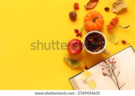 Composition with mug of berry tea, book and autumn decor on yellow background
