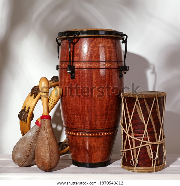 Composition of musical ethnic instrument. Maracas,\
tambourine, conga and ethnic drum. Percussion rhytm instruments are\
on white background with palm shade. Cuban sound, latin culture,\
samba and rumba