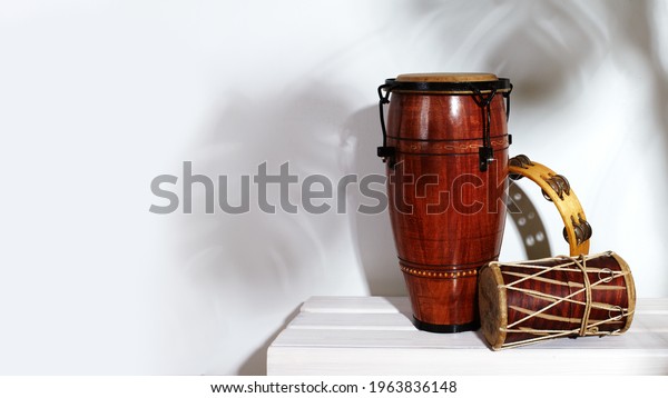 Composition of musical ethnic instrument. Maracas,\
tambourine, conga and ethnic drum. Percussion rhytm instruments are\
on white background with palm shade. Cuban sound, latin culture,\
samba and rumba