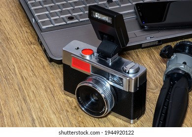 Composition of an old camera, tripod, mobile and computer on a table.