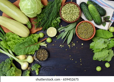 Composition On A Dark Background Of Green Organic Vegetarian Products: Green Leafy Vegetables, Mung Beans, Zucchini, Garlic, Onions, Cucumbers, Peppers, Lime. Top View. Green Food