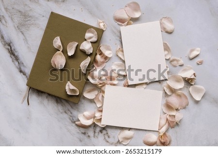 The composition on a flat surface of marble with empty white cards, a notebook and pink rose petals.  A layout for visualizing the design of postcards and paper printing.