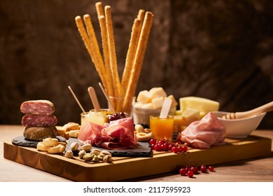 Composition on a wooden cutting board of cold cuts, cheeses, jams with mustard, berries and snacks in closeup - Powered by Shutterstock