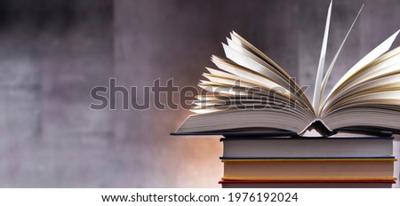 A composition with an open book lying on a stack of other books 