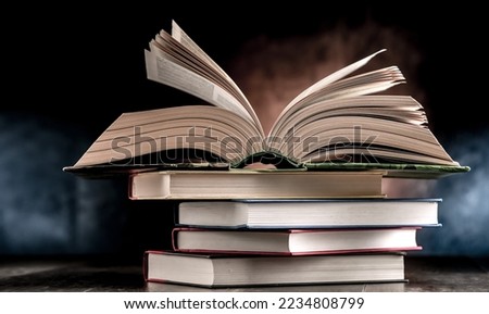 A composition with an open book lying on a stack of other books 