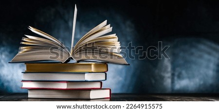A composition with an open book lying on a stack of other books 