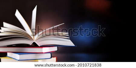 A composition with an open hardcover book lying on a stack of other books 