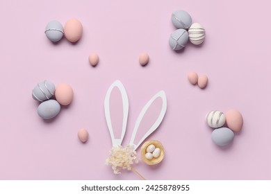 Composition with painted Easter eggs, nest and paper bunny ears on purple background - Powered by Shutterstock