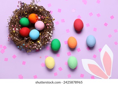 Composition with painted Easter eggs in wicker nest and paper bunny ears on purple background - Powered by Shutterstock