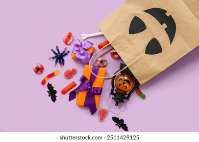 Composition with paper shopping bag, gifts and candies for Halloween on lilac background - Powered by Shutterstock