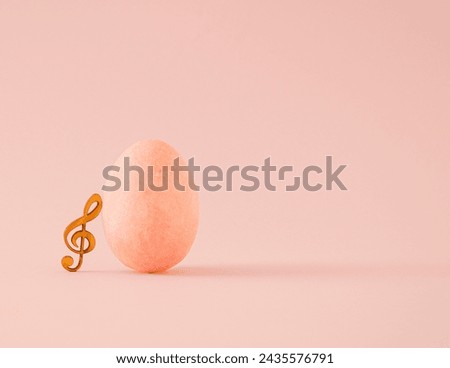 Composition of pastel orange egg and wooden treble clef. Minimal holiday Easter musical concept. Monochromatic colors. Copy space.