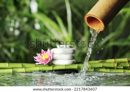 Composition with pebble, flower and bamboo fountain against blurred background