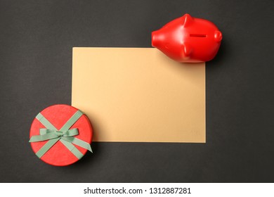 Composition With Piggy Bank, Blank Paper Sheet And Gift Box On Dark Background. Savings Concept