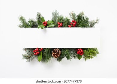 Composition of red holly berries and green branches on white background. Winter natural decoration. Botanical festive flat lay, top view.